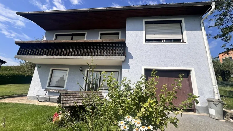 Zweistöckiges Haus mit hellblauer Fassade, Balkon und integrierter Garage unter blauem Himmel.