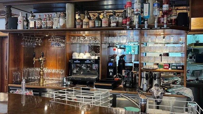 Elegante Bar mit Holztheke, reichhaltiger Getränkeauswahl und kunstvoller Deckenbeleuchtung in einem Café.