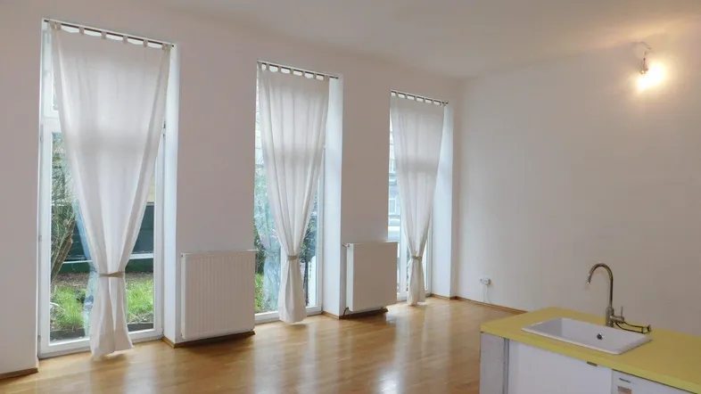 Heller Wohnbereich mit Holzboden, großen Fenstern und einer integrierten Küchenzeile mit Spüle.