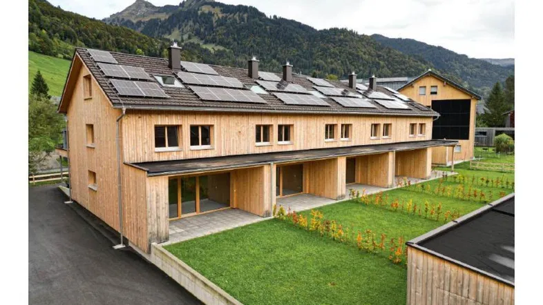 Moderne Reihenhäuser mit Holzfassade, Solaranlagen auf dem Dach und Blick auf die Berge.