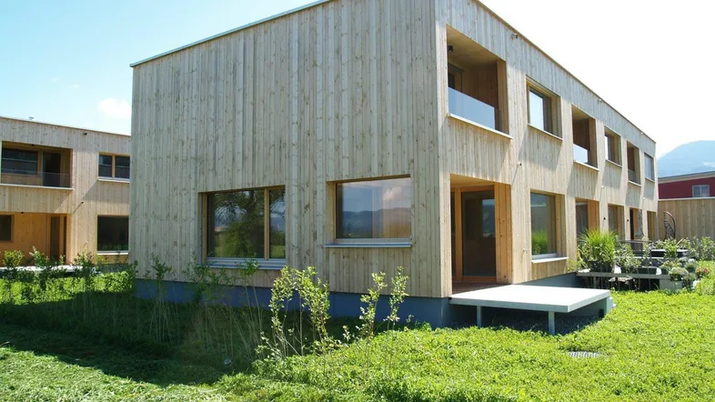 Modernes Holzhaus mit klarer Architektur, umgeben von einer grünen Wiese unter blauem Himmel.