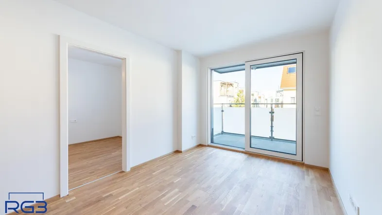 Helles Zimmer mit Parkettboden und Zugang zu einem Balkon, ideal als Wohn- oder Schlafbereich.