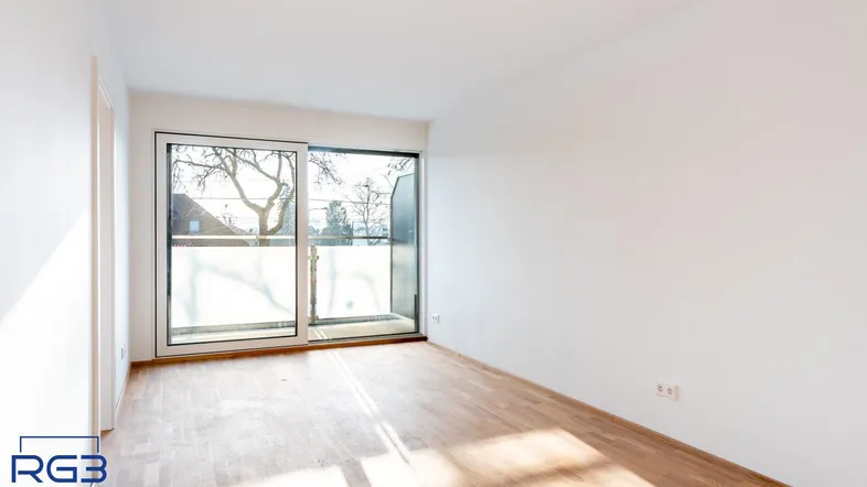 Helles Zimmer mit Holzboden und Zugang zu einem Balkon, ideal als Wohn- oder Schlafbereich.