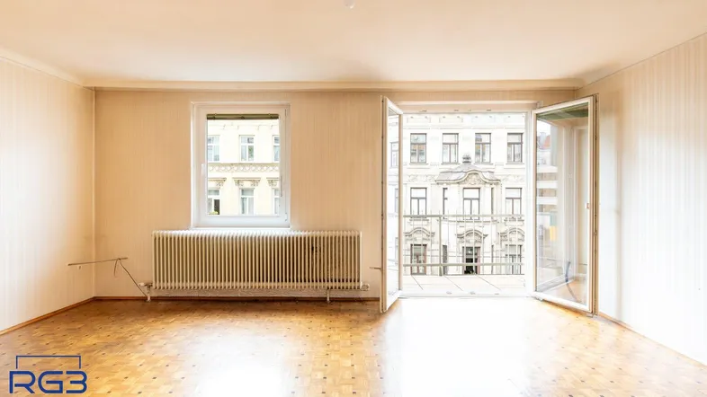 Geräumiges Wohnzimmer mit geöffneter Balkontür, Parkettboden und Blick auf die gegenüberliegenden Gebäude.