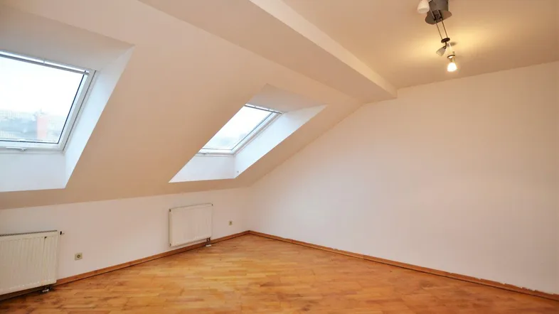 Helles Dachzimmer mit schrägen Wänden, zwei Dachfenstern und Parkettboden.