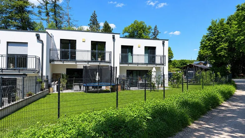 Moderne Reihenhäuser mit Balkonen, eigenem Garten und Trampolin in grüner Umgebung.