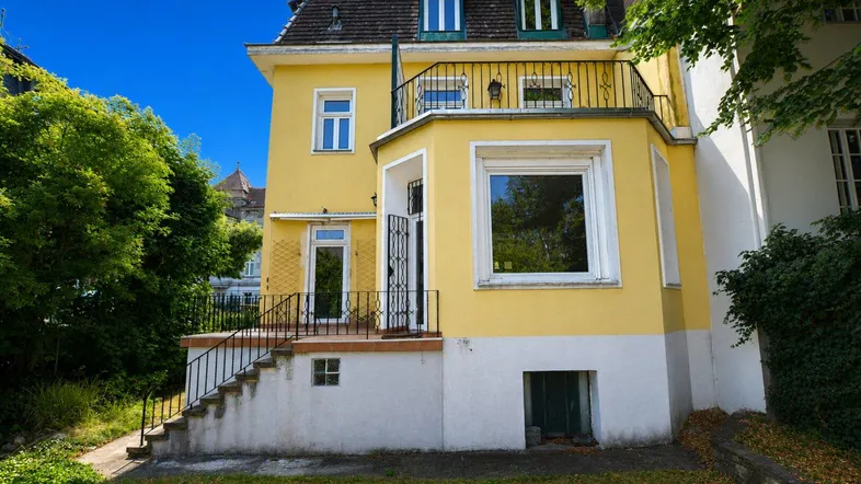 Gelbe Villa mit Mansarddach, Balkon und Zugang zum gepflegten Gartenbereich.