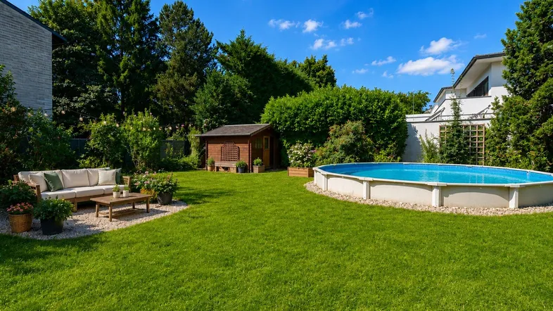 Gepflegter Garten mit Rasenfläche, gemütlicher Sitzecke, Gartenhaus und einem Aufstellpool.