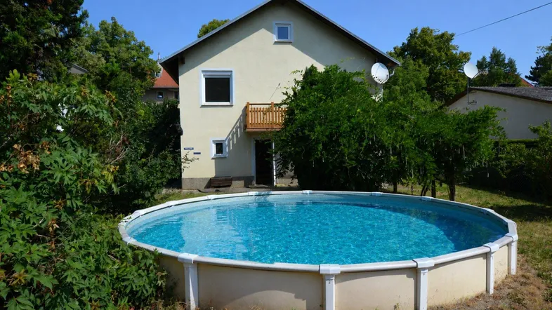 Haus mit Garten, Aufstellpool und kleinem Balkon unter blauem Himmel.