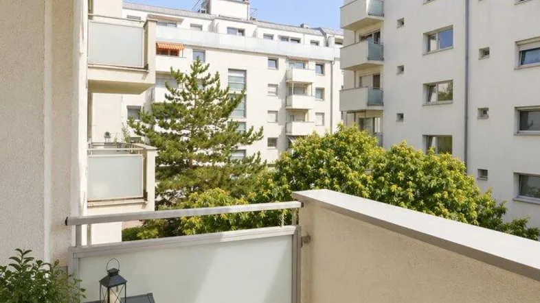 Heller Balkon mit Blick auf die umliegenden Wohngebäude und grüne Bäume.