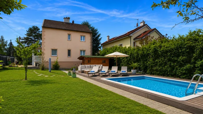 Haus mit großem Garten, Swimmingpool und Liegebereich unter blauem Himmel.