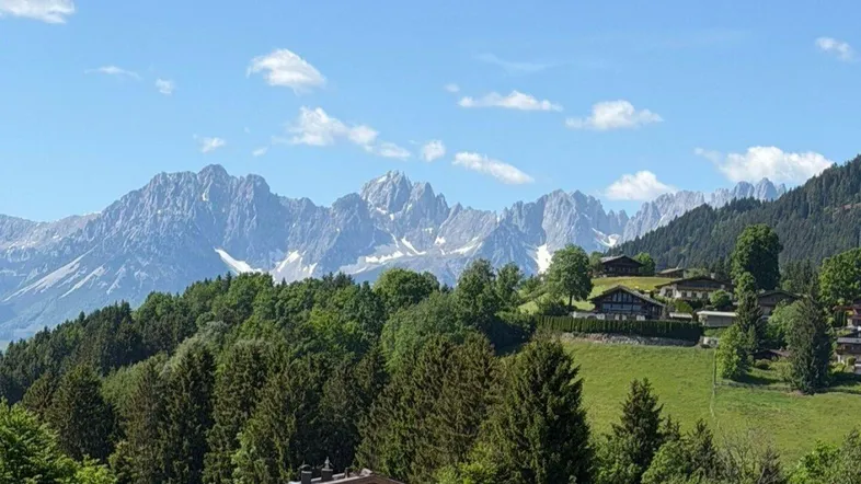 Panoramablick auf die majestätischen Berge und grüne Hügel mit traditionellen Häusern unter blauem Himmel.