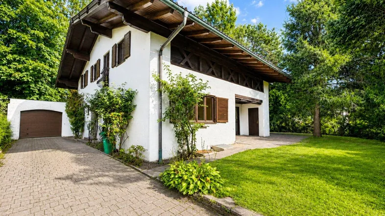 Traditionelles Haus mit weißer Fassade, Holzdetails, gepflasterter Auffahrt und Garage.