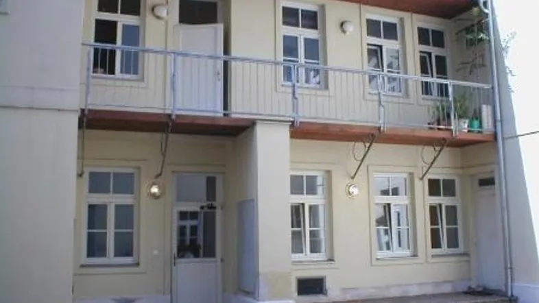 Hintere Fassade eines Gebäudes mit einem durchgehenden Balkon und mehreren Fenstern.