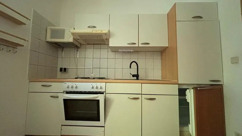 Kleine Einbauküche mit weißen Schränken, Herd, Spüle und Mikrowelle, funktional eingerichtet.