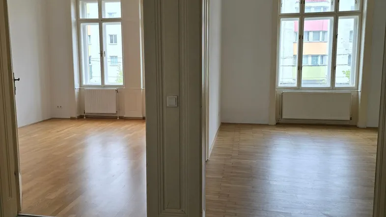 Helle, leere Räume mit Parkettboden und großen Fenstern, die viel Tageslicht hereinlassen.