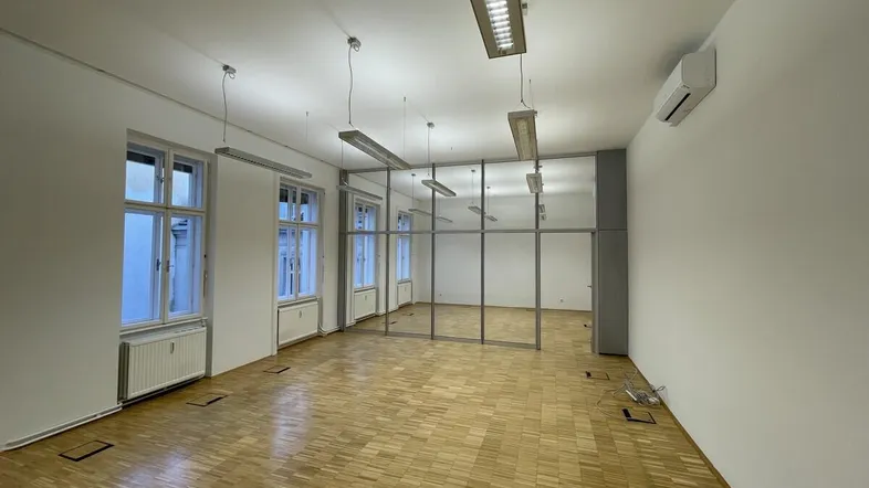 Geräumiger Büroraum mit Parkettboden, großen Fenstern und modernen Glasabtrennungen.