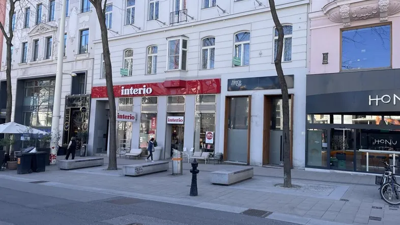 Eine belebte Geschäftsstraße mit mehreren Ladenfronten und einem klassischen Gebäude im Hintergrund.