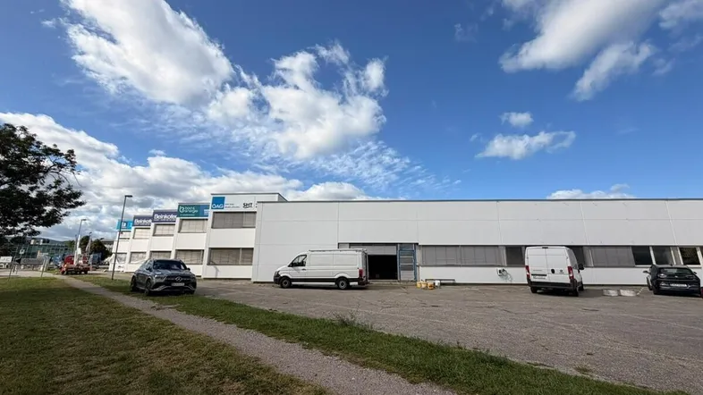 Gebäudeansicht eines Gewerbeobjekts mit Parkplätzen und Lieferwagen unter blauem Himmel.