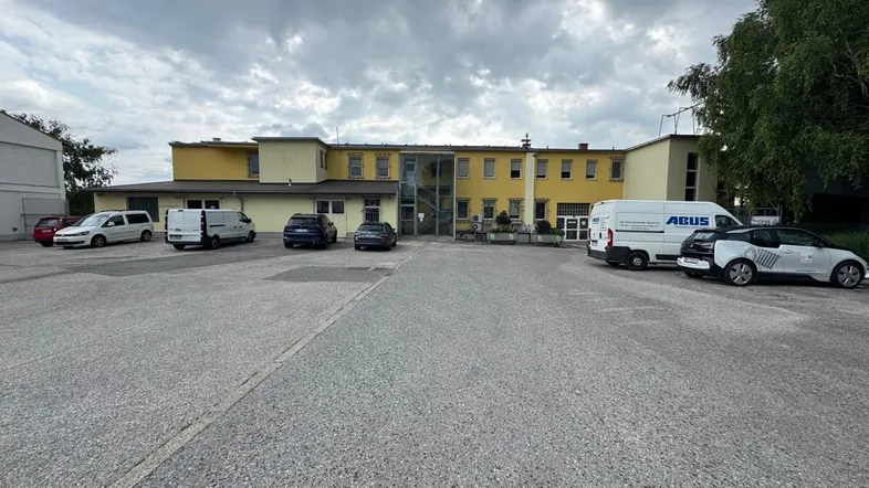 Gelbes Geschäftsgebäude mit großem Parkplatz und mehreren Fahrzeugen unter bewölktem Himmel.
