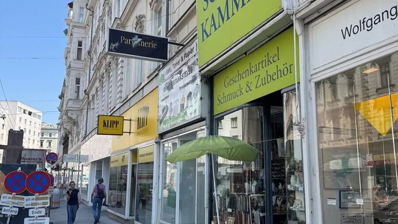 Blick auf die belebte Geschäftsstraße mit verschiedenen Ladenlokalen im Erdgeschoss eines Altbaus.