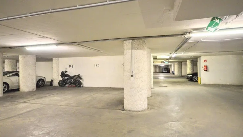 Geräumige Tiefgarage mit Betonboden und Säulen, beleuchtet mit Leuchtstoffröhren und einigen Fahrzeugen.