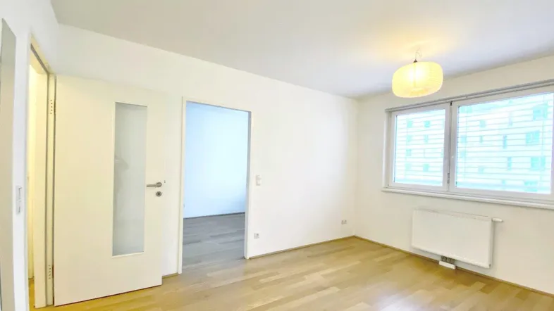 Helles Zimmer mit Parkettboden und Fenster, ideal als Schlaf- oder Wohnbereich.