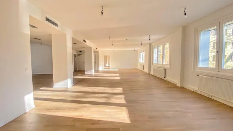 Heller, großer Raum mit Holzboden und vielen Fenstern, ideal für Büronutzung oder offenes Wohnen.