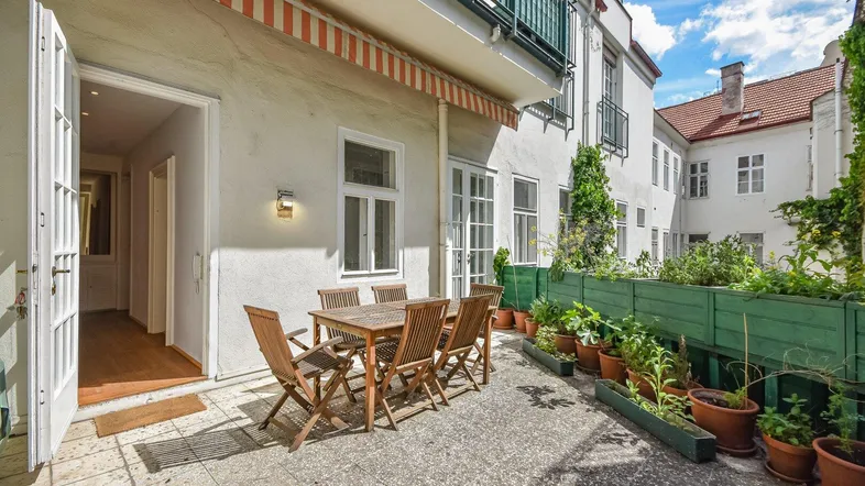 Eine einladende Terrasse mit Holztisch und Stühlen, umgeben von Pflanzen in Töpfen.