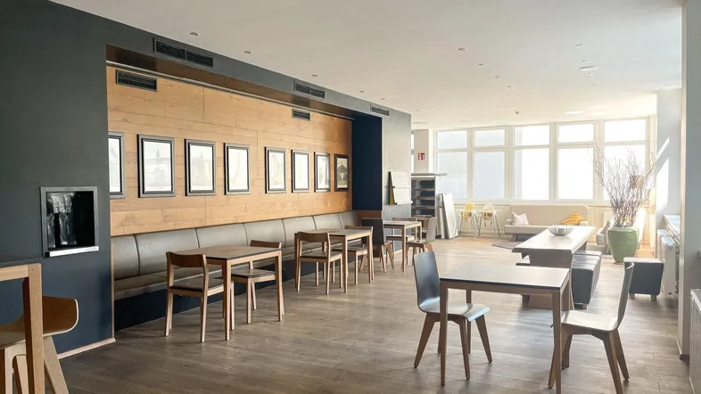 Geräumiger Loungebereich mit Holzboden, langer Sitzbank und großen Fenstern, ideal für Gemeinschaftsaktivitäten.