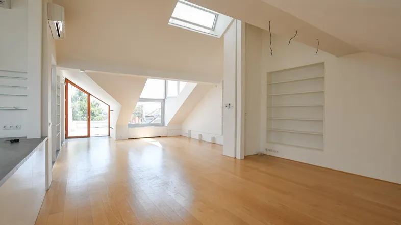 Helles Dachgeschoss-Wohnzimmer mit Holzboden, großen Fenstern und eingebauten Regalen.