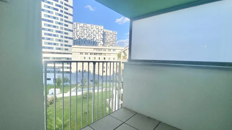 Heller Balkon mit Fliesenboden und Blick auf moderne Gebäude und Grünflächen.