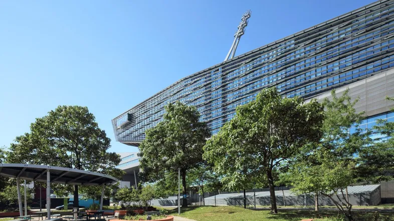 Modernes Bürogebäude mit markanter Architektur und umliegender Grünfläche unter blauem Himmel.