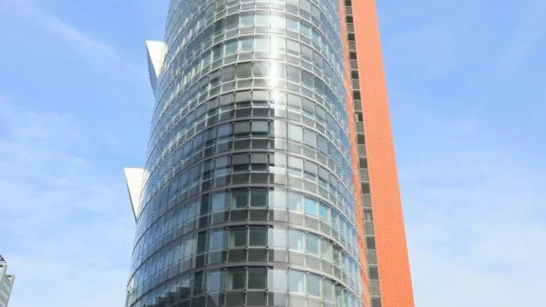 Modernes Hochhaus mit einer beeindruckenden Glasfassade und schlanker Architektur unter blauem Himmel.