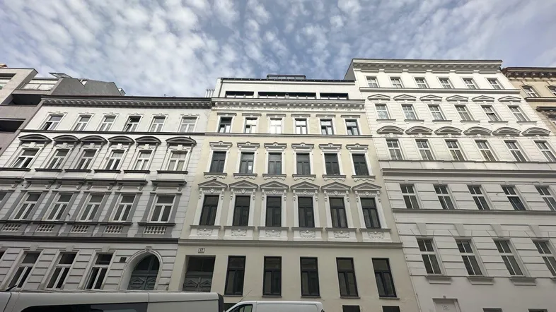 Historische Fassade eines Mehrfamilienhauses in der Stadt mit modernen Dachaufbauten.