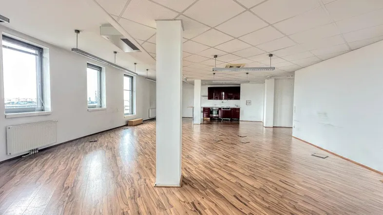 Geräumiges Großraumbüro mit Holzboden, abgehängter Decke und integrierter Küchenzeile, hell durch große Fenster.