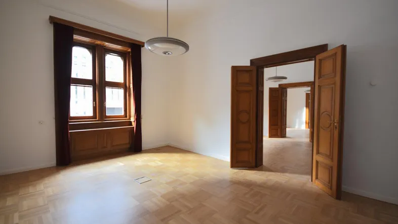 Geräumiges Zimmer mit Fischgrätparkett, hohen Decken und großen Holzfenstern, die viel Tageslicht hereinlassen.