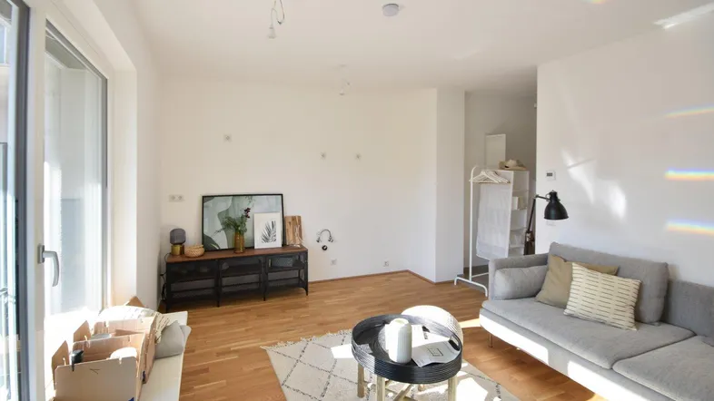 Helles Wohnzimmer mit Holzboden, großem Fenster und moderner Einrichtung, bereit zum Einzug.