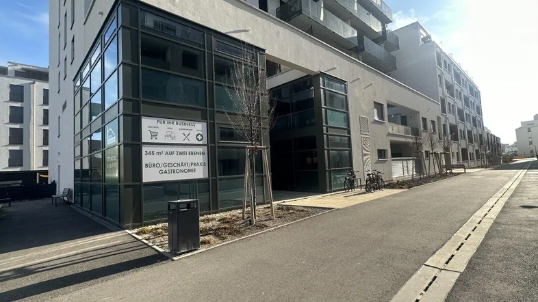 Moderne Geschäftsfassade eines Neubaus mit großen Glasflächen und umliegender Straße.