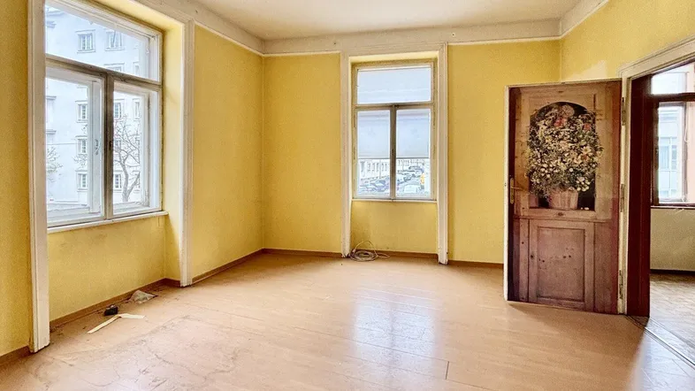 Helles Wohnzimmer mit gelben Wänden, Holzboden und zwei großen Fenstern zur Straße.