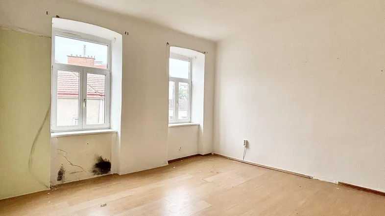 Heller Raum mit Renovierungsbedarf, sichtbaren Feuchtigkeitsschäden und Holzboden.
