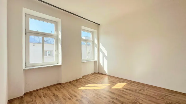 Helles Zimmer mit Laminatboden und zwei Fenstern, das viel Tageslicht hereinlässt.
