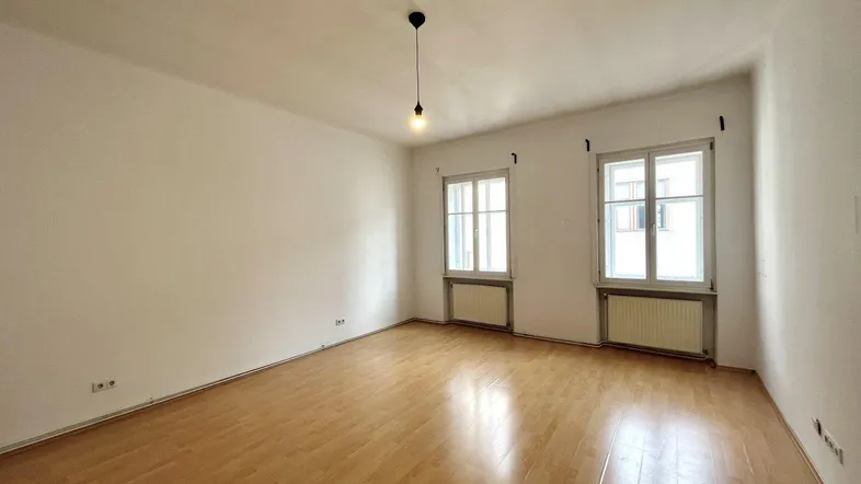 Helles Zimmer mit Parkettboden, weißen Wänden und zwei Fenstern, bereit zur individuellen Gestaltung.