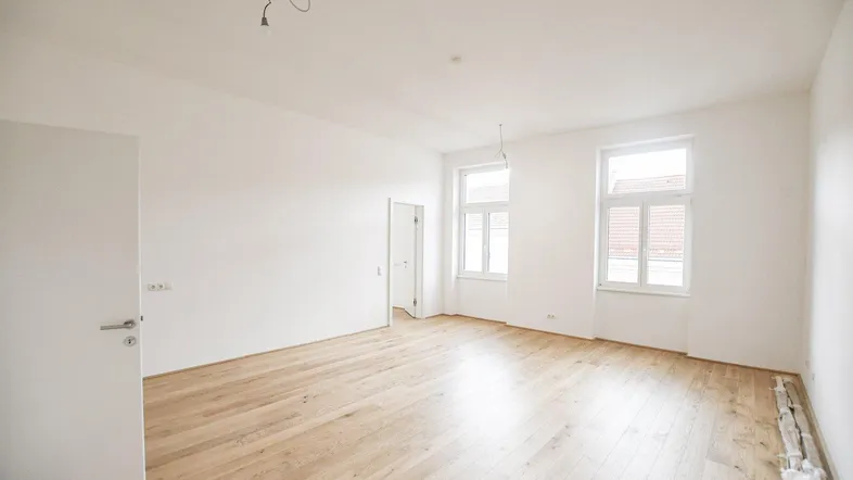 Helles, leeres Zimmer mit weiß gestrichenen Wänden und neuem Holzparkettboden.