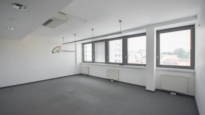 Geräumiges, leeres Büro mit Teppichboden, großen Fenstern und viel Tageslicht.