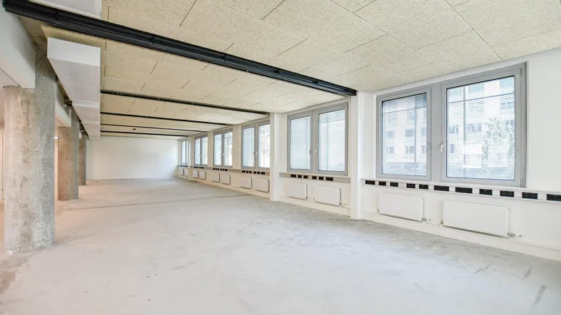 Geräumiger, unmöblierter Büroraum mit großen Fenstern, Akustikdecke und Betonstützen.