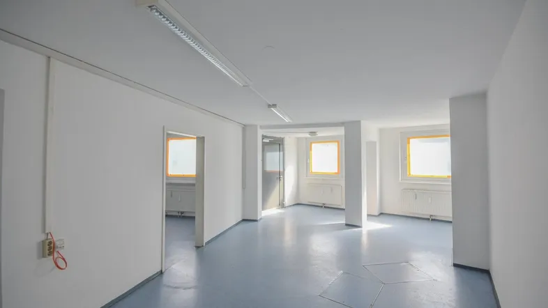 Heller Büroraum mit blaugrauem Vinylboden, weißen Wänden und mehreren Fenstern, die viel Tageslicht hereinlassen.
