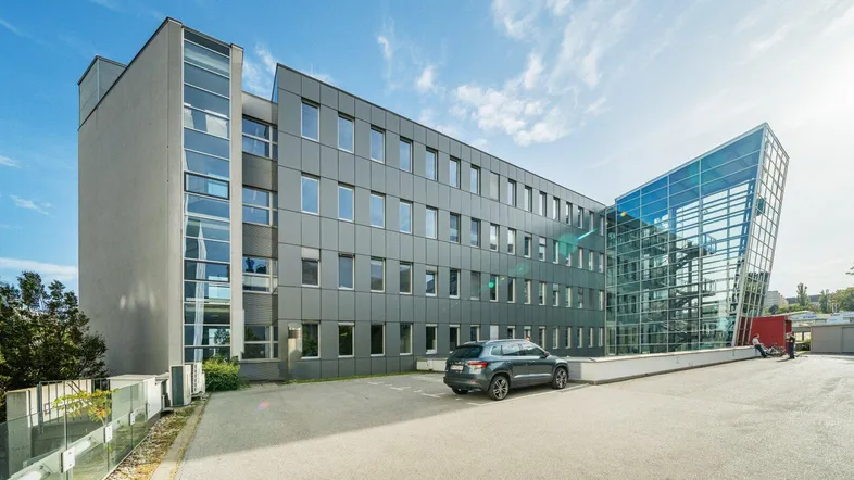 Modernes Bürogebäude mit Glasfassade und Parkplatz unter blauem Himmel.