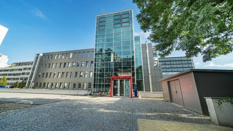 Modernes Bürogebäude mit Glasfassade und gepflastertem Vorplatz unter blauem Himmel.
