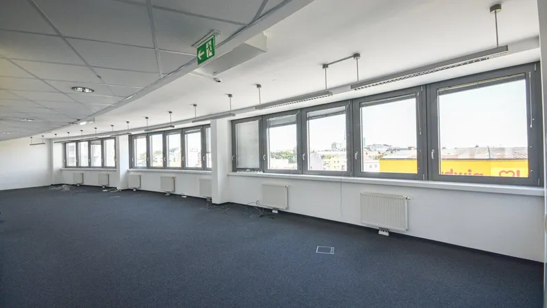 Geräumiges, leeres Büro mit vielen Fenstern, Teppichboden und Blick auf die Stadt.